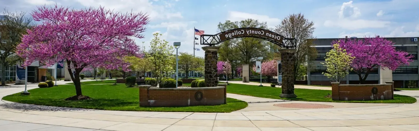 Campus photo of the Ocean County College arch with flowering trees in spring